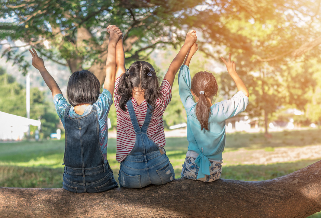Children friendship concept with happy girl kids in the park having fun sitting under tree shade playing together enjoying good memory and moment of student lifestyle with friends in school time day (Children friendship concept with happy girl kids in